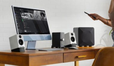 A modern wooden desk with a computer setup featuring a large monitor displaying a music playlist titled