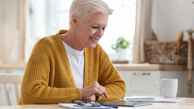 An older woman sitting at her dining table, smiling as she works