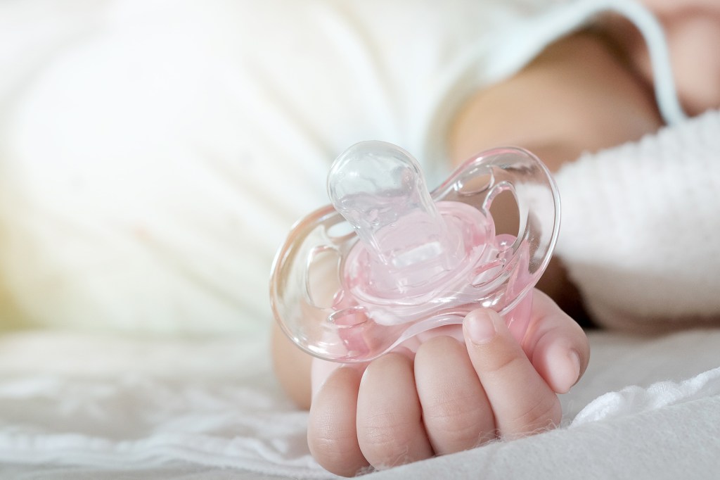 Close-up of a baby's hand holding a pink pacifier.