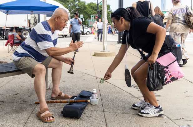 Busker Zhen Jinling, left, thanks a passerby for giving him money while he plays traditional Chinese folk music on the Suona, a horn instrument, in Chinatown on July 27, 2025, in Chicago. (Dominic Di Palermo/Chicago Tribune)