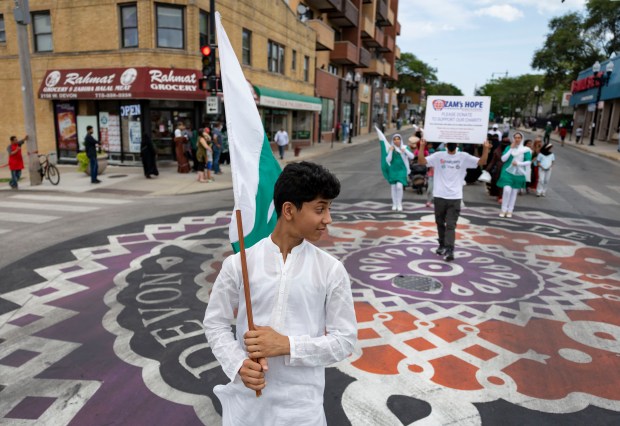 Azair Arkum holds a flag while marching down West Devon Avenue to celebrate Pakistan Independence Day on Aug. 10, 2025, in the West Rogers Park neighborhood of Chicago. The annual event, complete with floats and music, commemorates the day Pakistan achieved independence from the British colonial rule in 1947. (Brian Cassella/Chicago Tribune)