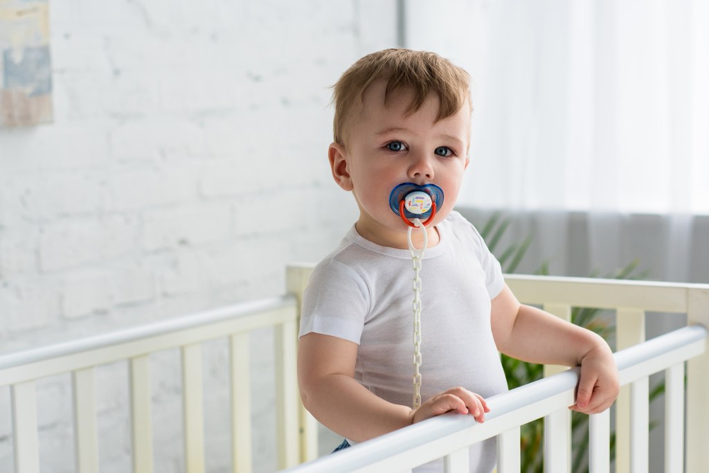 Baby boy with pacifier in crib.