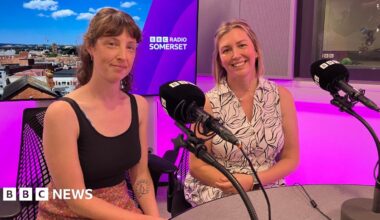 Lucy Sheppard and Aimee Peach sit next to each other in the BBC Radio Somerset studio. Lucy is wearing a black top and a skirt with a flowery pattern and Aimee is wearing a black and white dress. The studio is lit up in purple colours.