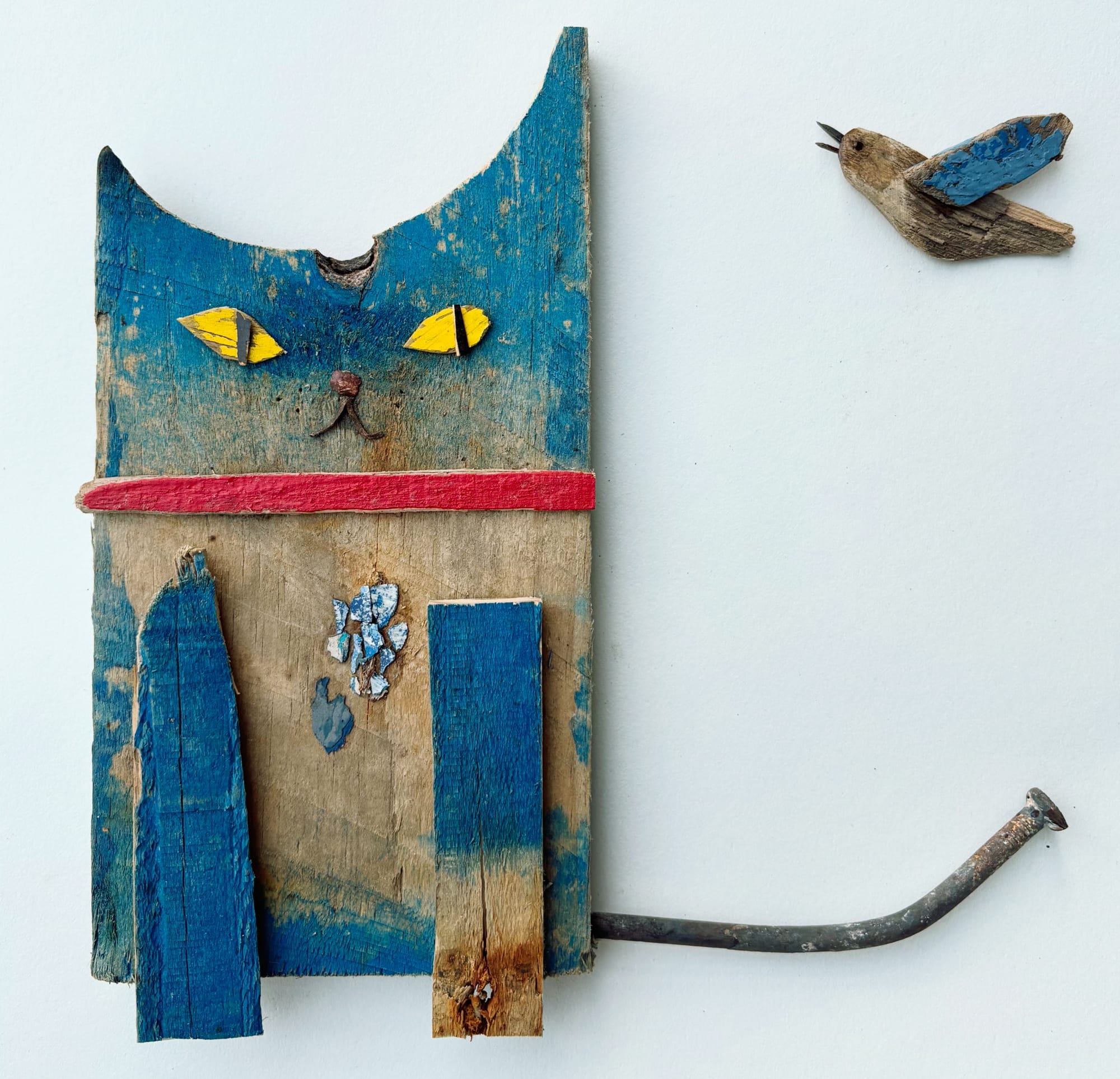 a cat and hummingbird sculpture made of worn blue and brown wood