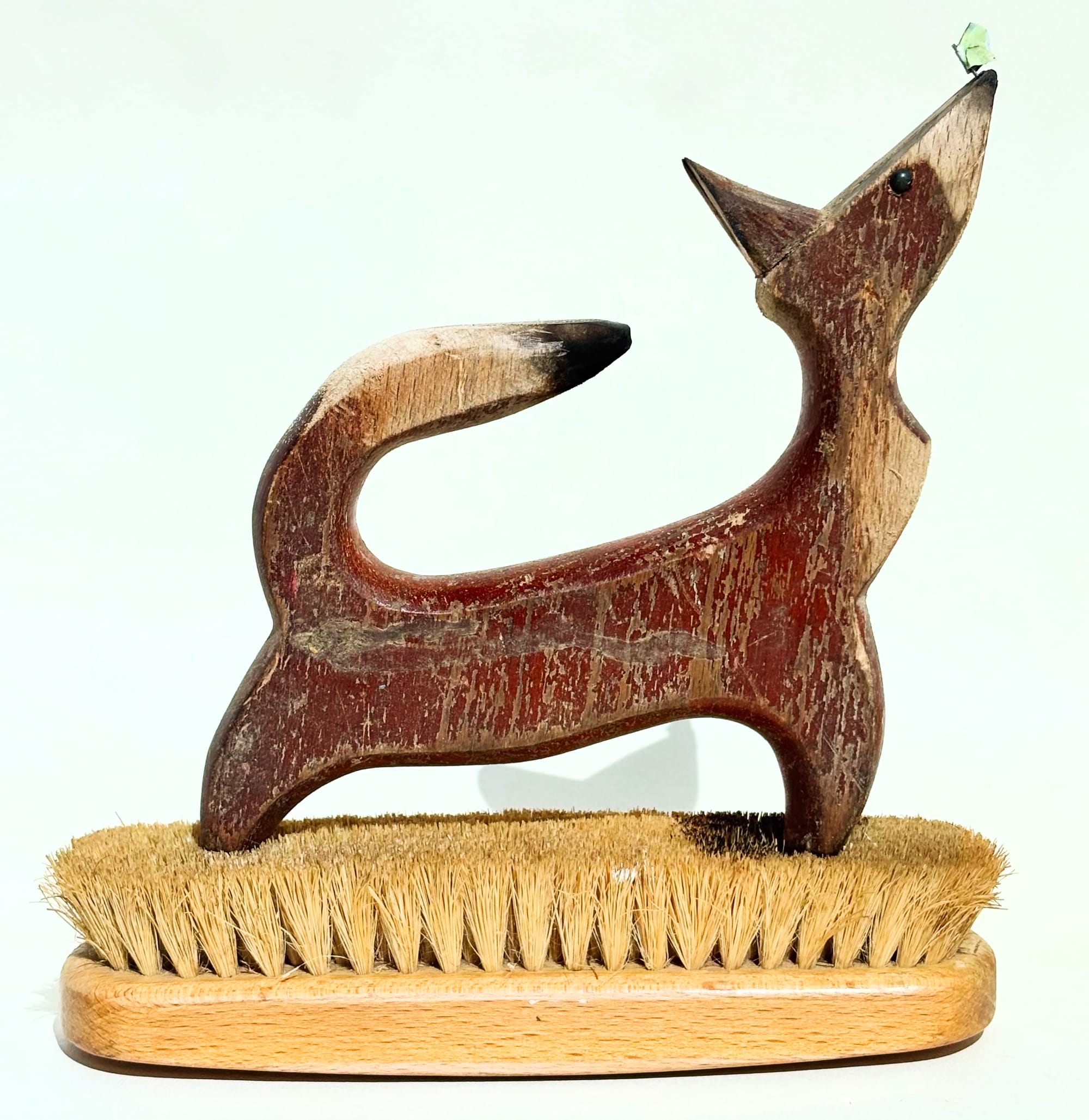 a dog sculpture made of worn red-brown wood atop a brush