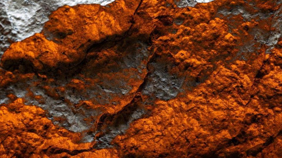A close-up of the meteorite glowing sliver and red. It resembles a mountainous landscape shot from above.