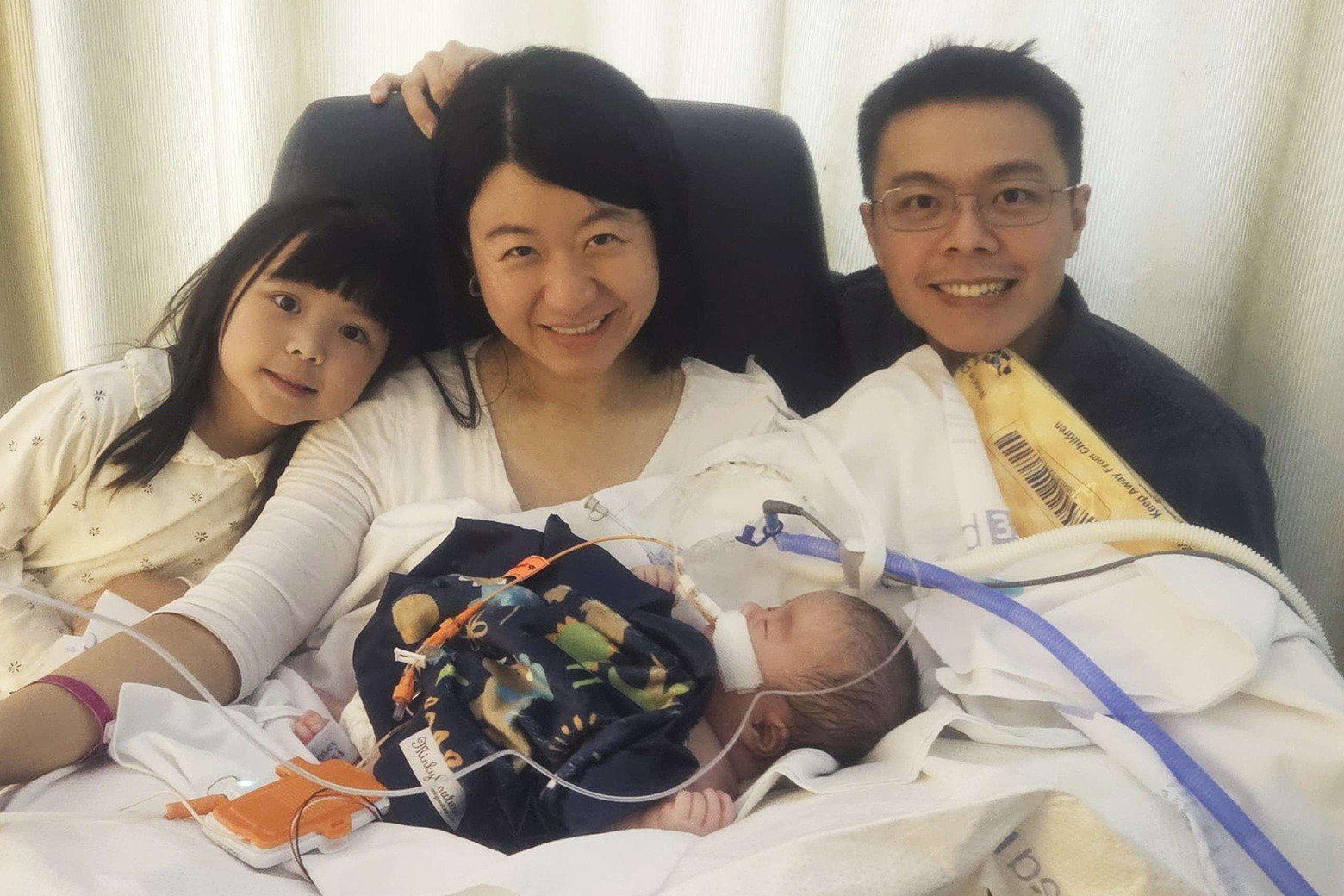 Woman, center, holds a baby in her arms as she sits between a young girl and a man with glasses
