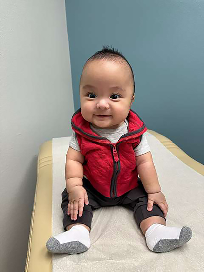 Baby in red zippered vest, black leggings and white socks seated on an examination table