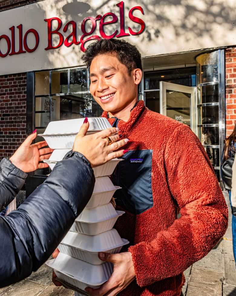 A customer distributes a stack of Apollo Bagels orders to his friends outside the restaurant.