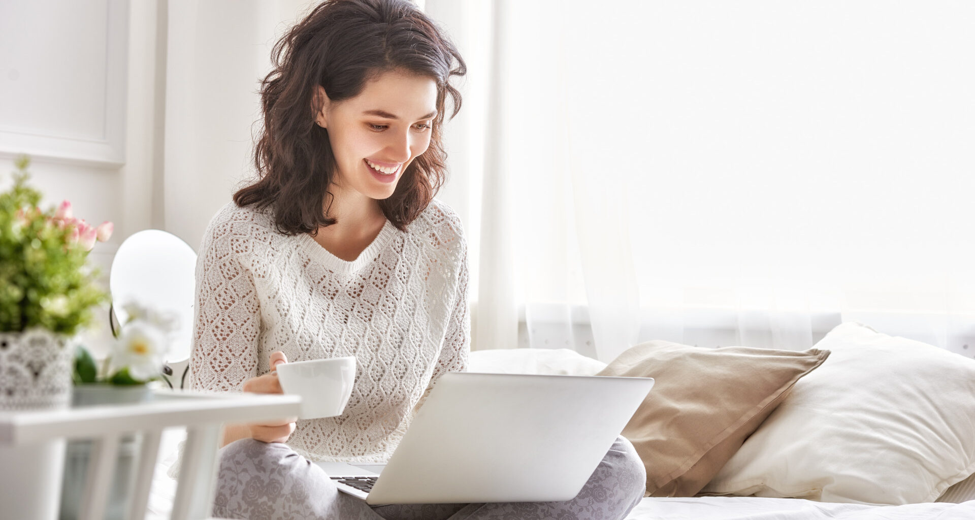 Happy woman sitting on a bed with a coffee and a Windows 10 laptop