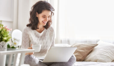 Happy woman sitting on a bed with a coffee and a Windows 10 laptop