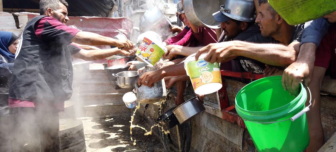 A group of displaced Palestinians gathering in front of a local community kitchen in western Gaza City.