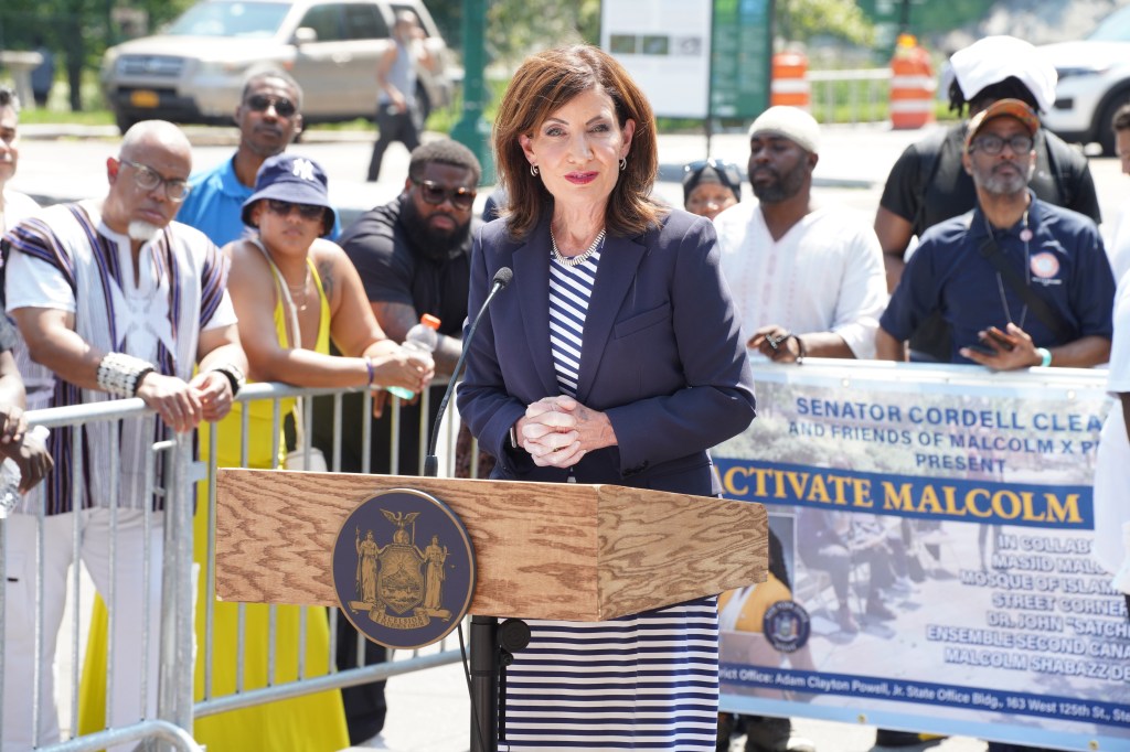 Kathy Hochul speaking at a podium at the renaming of the 110th Street train station.