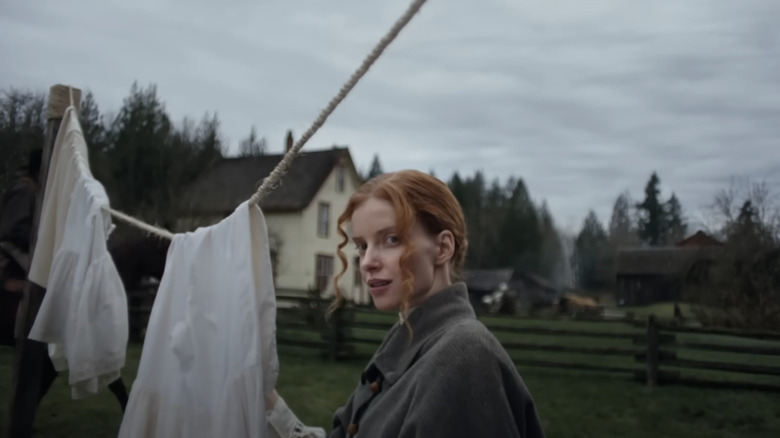 Claire Friesen as Ada in Keeper, seemingly living some time closer to the 1600s or 1700s, standing by a clothesline in front of an old-looking house looking into the camera.