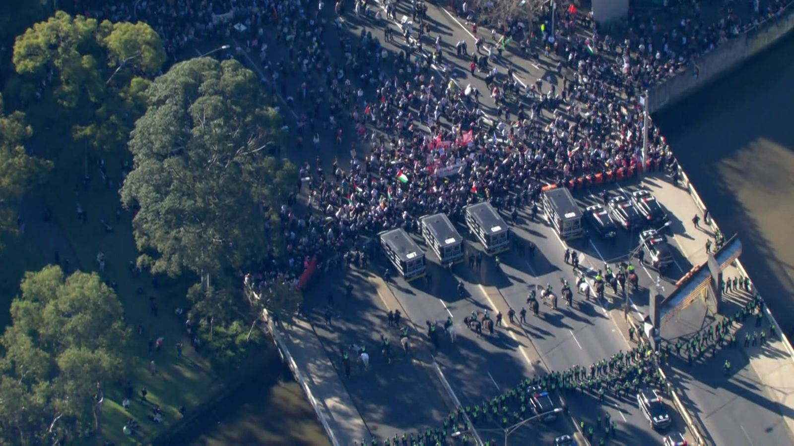 An aeriol shot of a large number of people press up against a line of riot police, black police vans and another row of police.