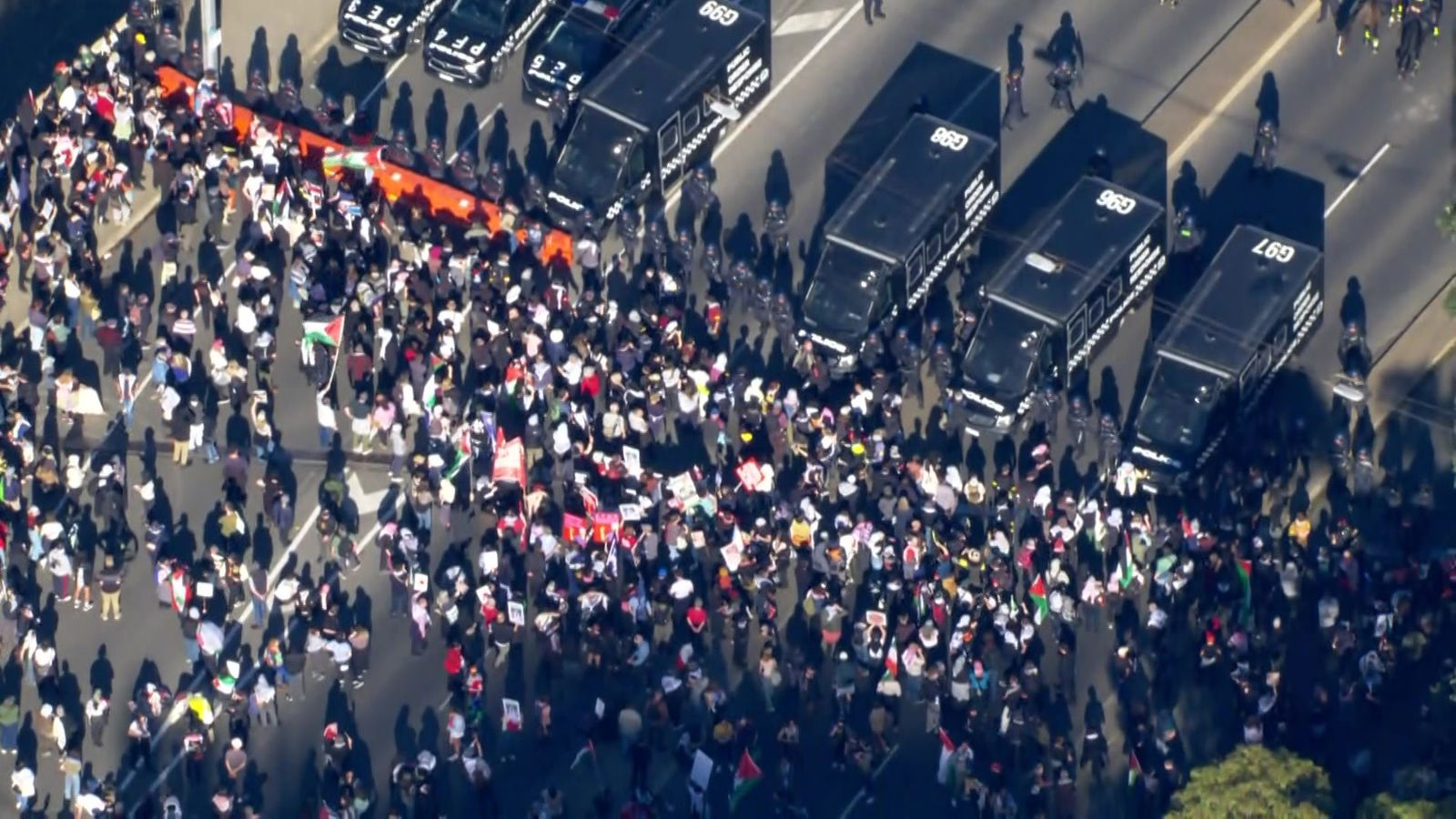 An aerial shot of a large number of people standing on a road facing a row of riot police and black police vans.