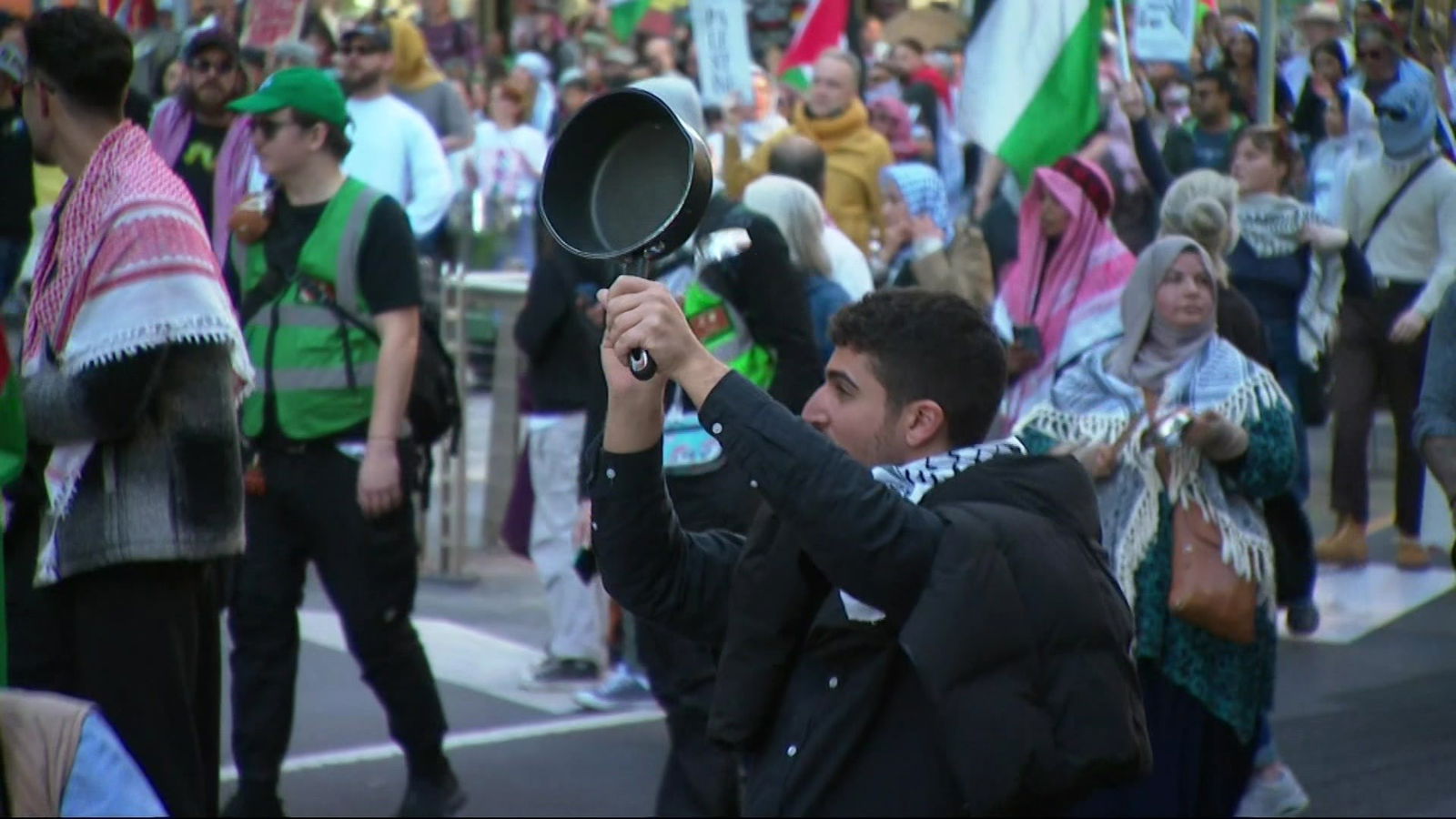A man holds up a saucepan as he walks with people carrying Palestinian flags.