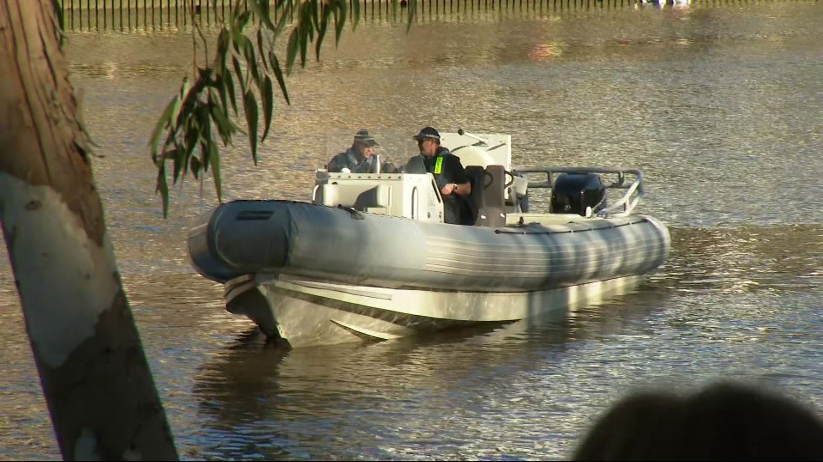 Two police officers in a rubber boat on a brown river.
