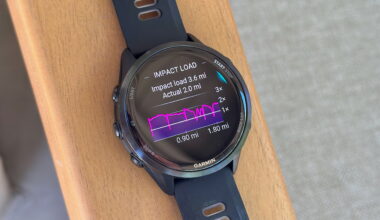 The Garmin Forerunner 970 sitting on an armrest showing the impact load graph for a track workout compared to the actual mileage, with some portions generating double the impact.