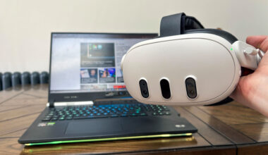 Meta Quest 3 held in hand with laptop on table in the background