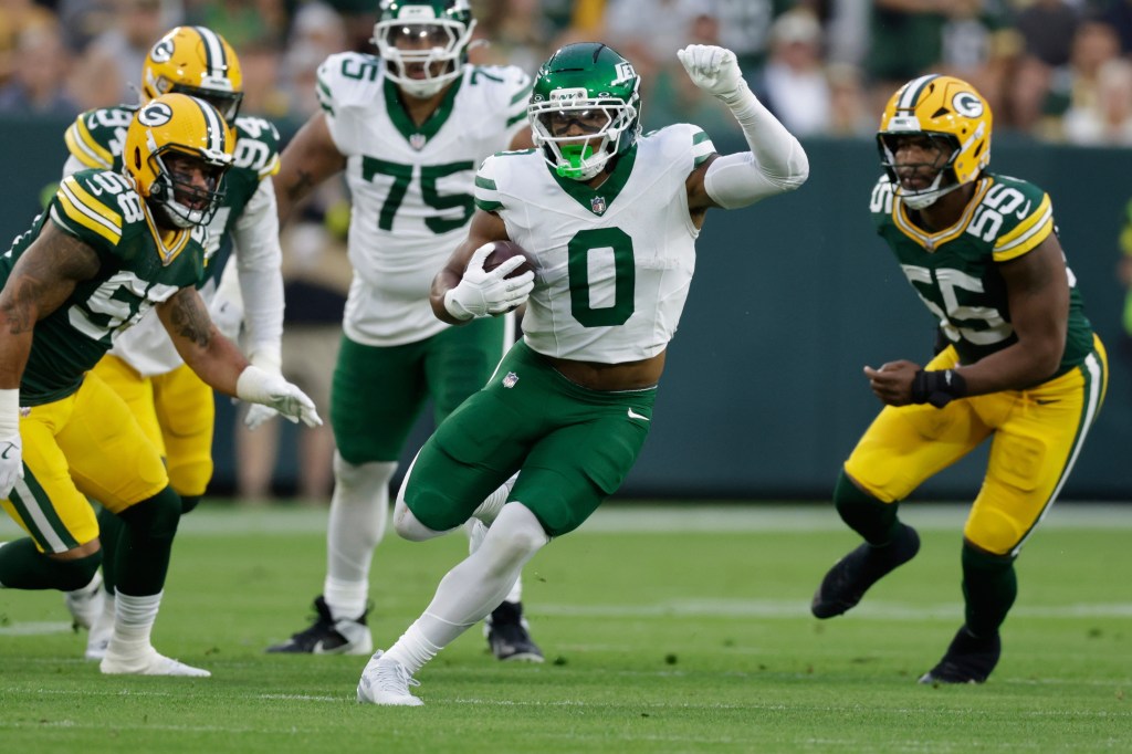 New York Jets player running with the football during a game against the Green Bay Packers.