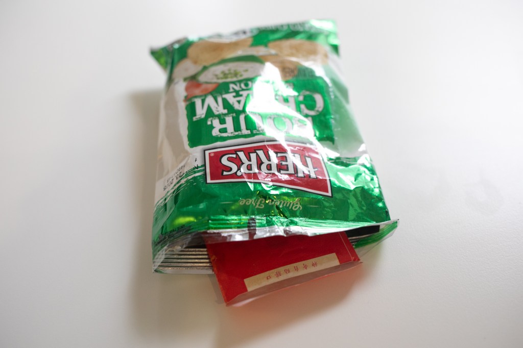 An open bag of Herr's Sour Cream and Onion potato chips with an envelope inside.