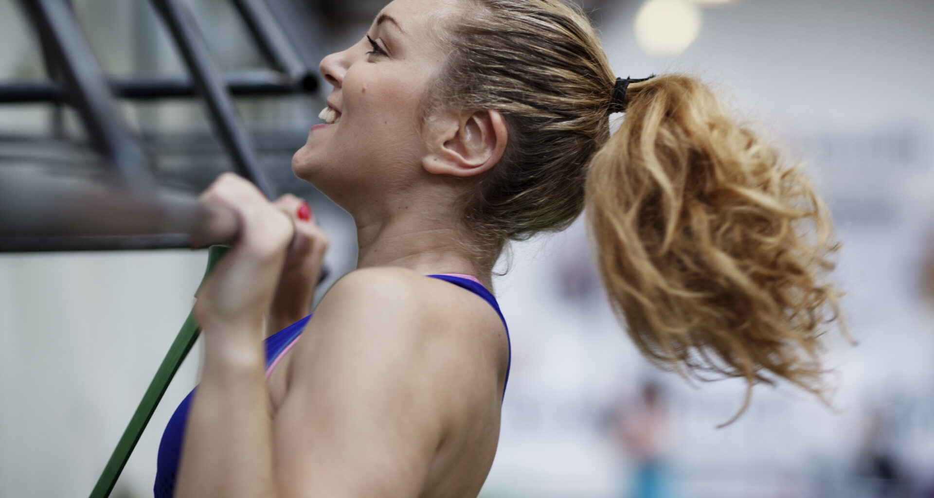 Smiling woman performing a pull-up in a gym, with her chin above the bar