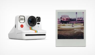 A white instant camera with rainbow stripes is shown next to a developed instant photo of a baseball game on a stadium field. The camera and photo are on a plain white background.