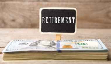 Stack of cash in front of a small black sign with white writing that reads 'retirement' against a wooden background
