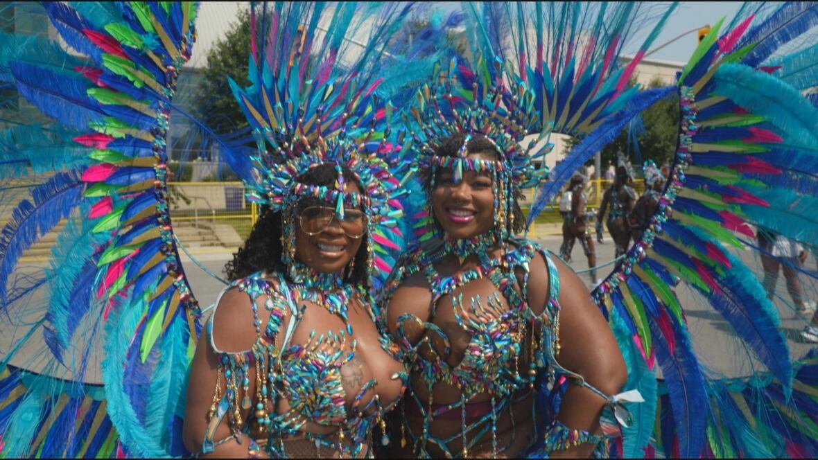 Revellers wearing large blue and green feathered costumes with jewels at a carnival.
