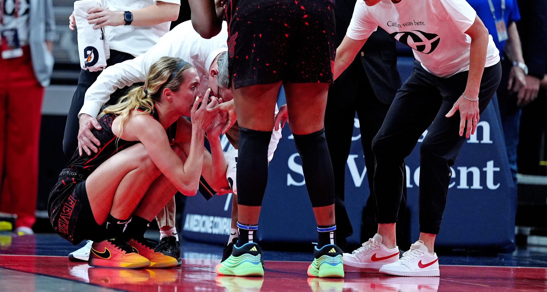 Lexie Hull crouches on the court, surrounded by concerned team staff and players, showing support and care.