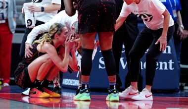Lexie Hull crouches on the court, surrounded by concerned team staff and players, showing support and care.