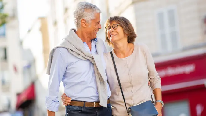 Smiling older couple walking arm-in-arm outdoors, symbolizing retirement planning, financial freedom, and enjoying life after reaching savings goals.