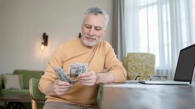 Gray-haired man standing and counting money stock photo