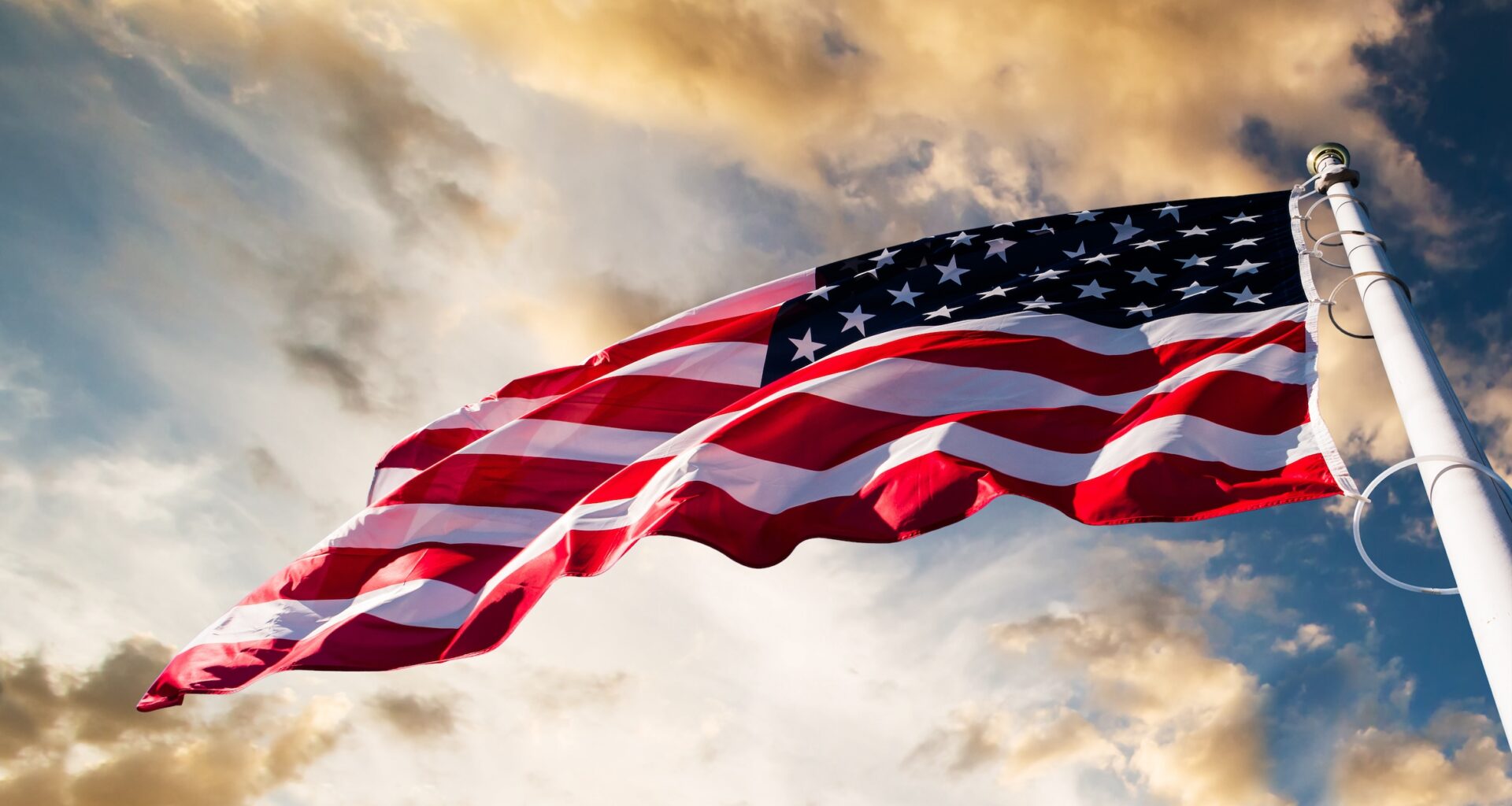 An American flag blowing in the wind with a blue sky and clouds