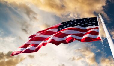 An American flag blowing in the wind with a blue sky and clouds