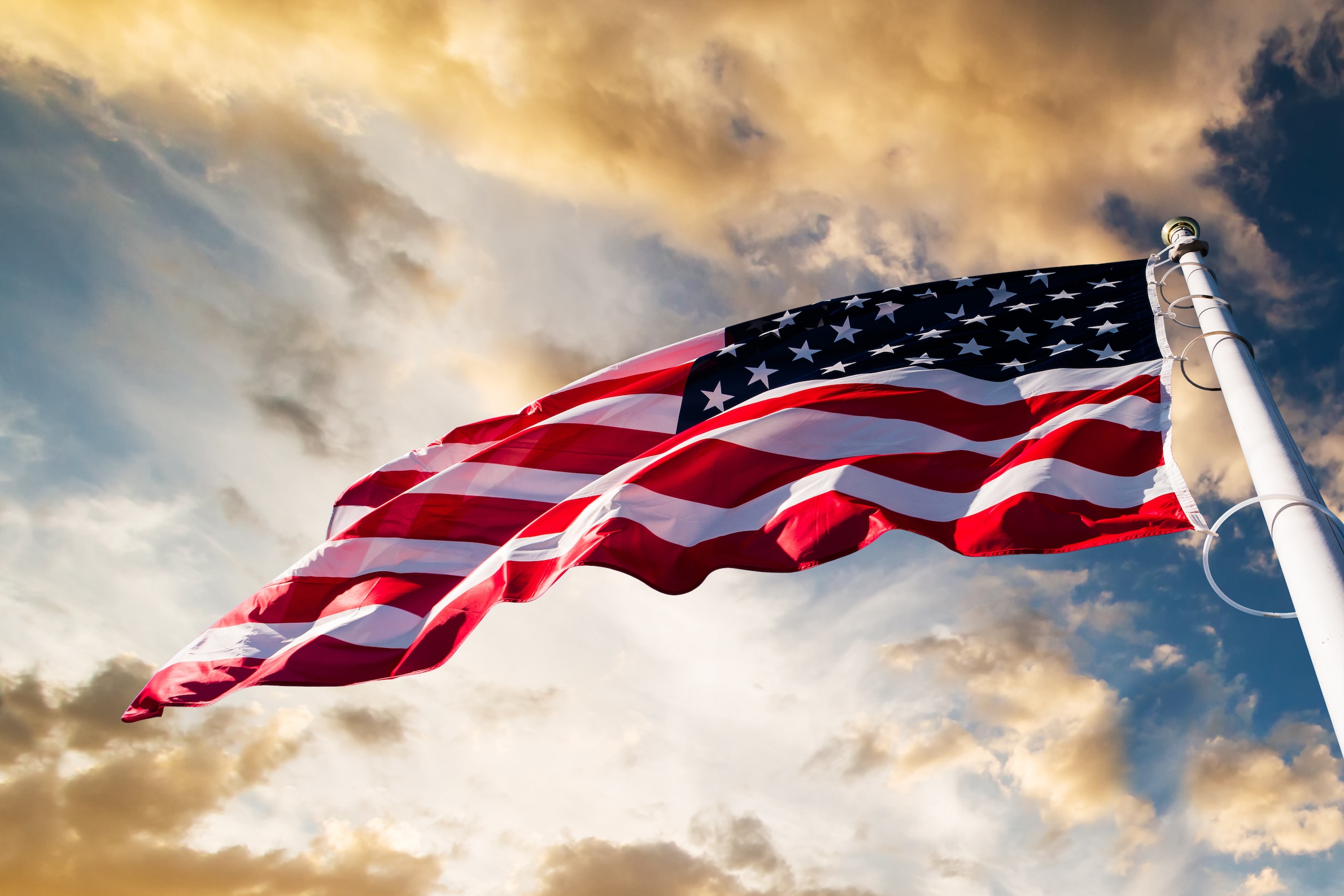 An American flag blowing in the wind with a blue sky and clouds
