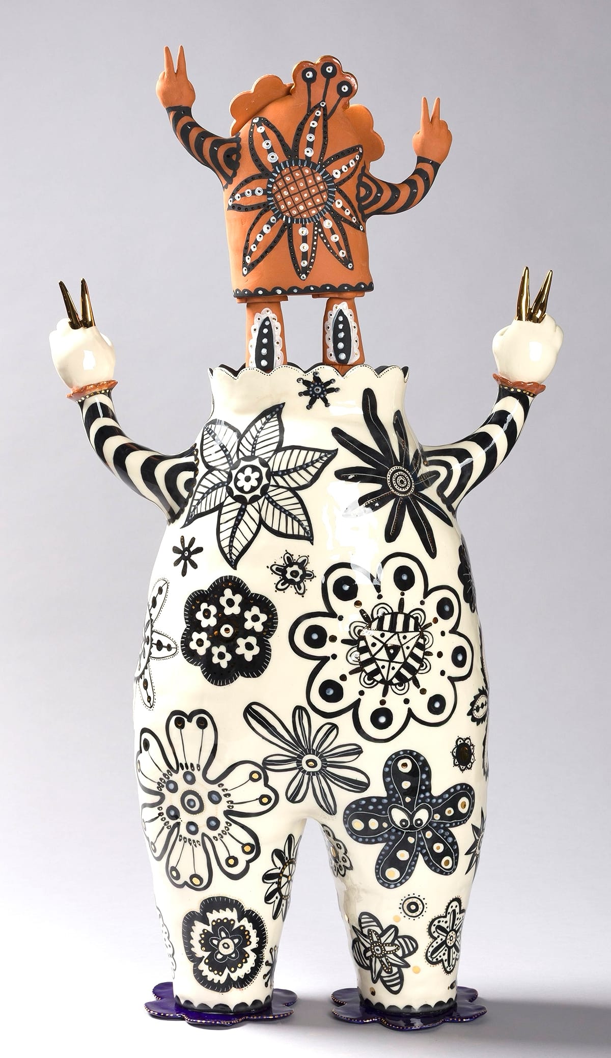 a white figure with black drawn patterns on its body and a tiny terracotta figure for a head. both have peace sign fingers