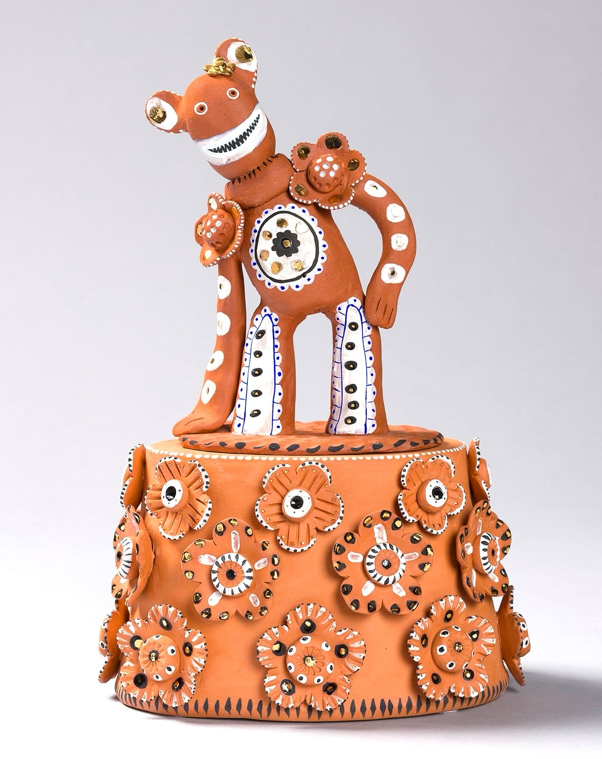 a terracota figure with patterns on its body and a wide smiling standing with a side bend on a base with flowers