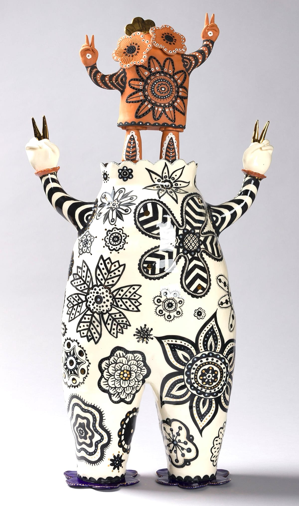 a white figure with black drawn patterns on its body and a tiny terracotta figure for a head. both have peace sign fingers
