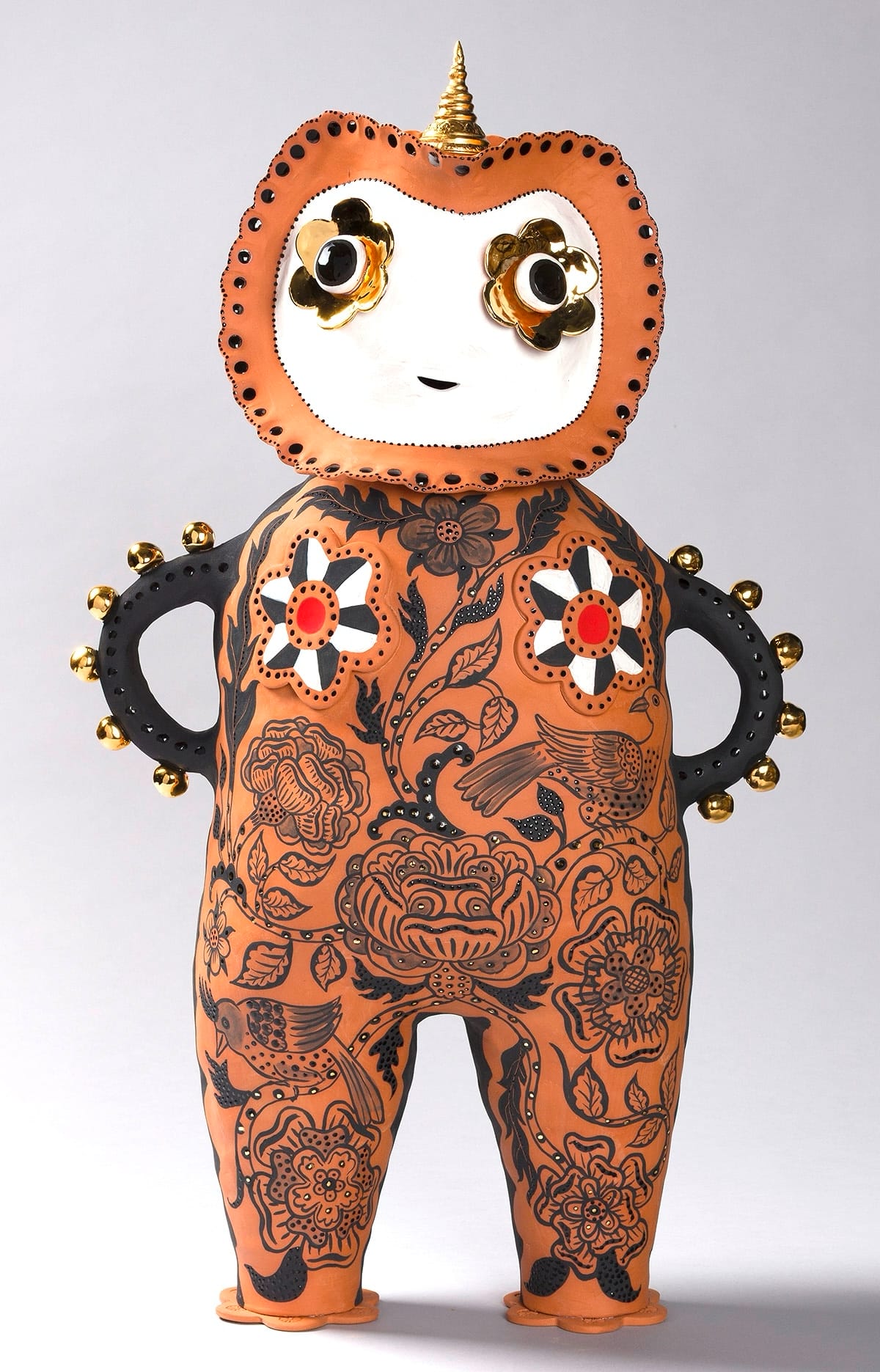 a terracotta figure with black drawings on its body, arms on its hips, and a white head