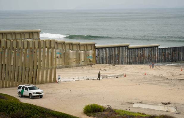 A Border Patrol officer walks down to ask a couple to step away from the primary fence in Border Field State Park. (Alejandro Tamayo / The San Diego Union-Tribune)
