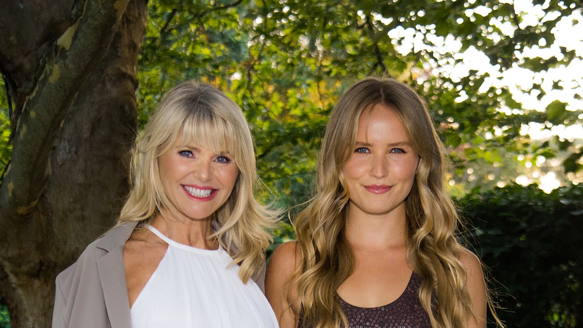 A close-up of Christie Brinkley wearing a white dress and a grey jacket with Sailor Brinkley Cook wearing a dark sleeveless dress outdoors.