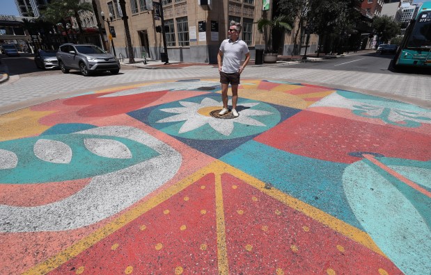 SKIP, the artist that created the murals on the roads throughout downtown Orlando, poses for a photo at the intersection of Orange Avenue and and Church Street in downtown Orlando, on Wednesday, Aug. 27, 2025. (Ricardo Ramirez Buxeda/Orlando Sentinel)