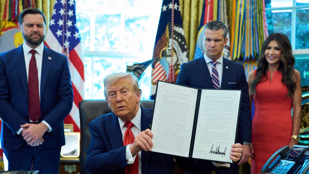 President Donald Trump holds up an executive order on cashless bail as Vice President JD Vance, from left, Defense Secretary Pete Hegseth and Homeland Security Secretary Kristi Noem look on in the Oval Office of the White House, Monday, Aug. 25, 2025, in Washington. (AP Photo/Evan Vucci)