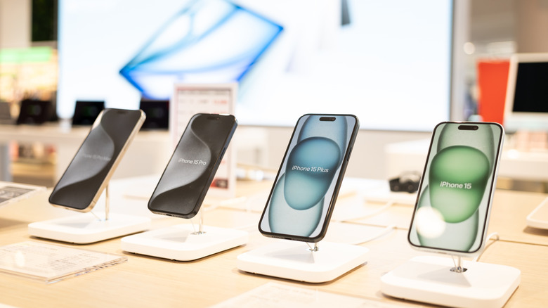 A row of iPhone 15 devices displayed on a table at a store.