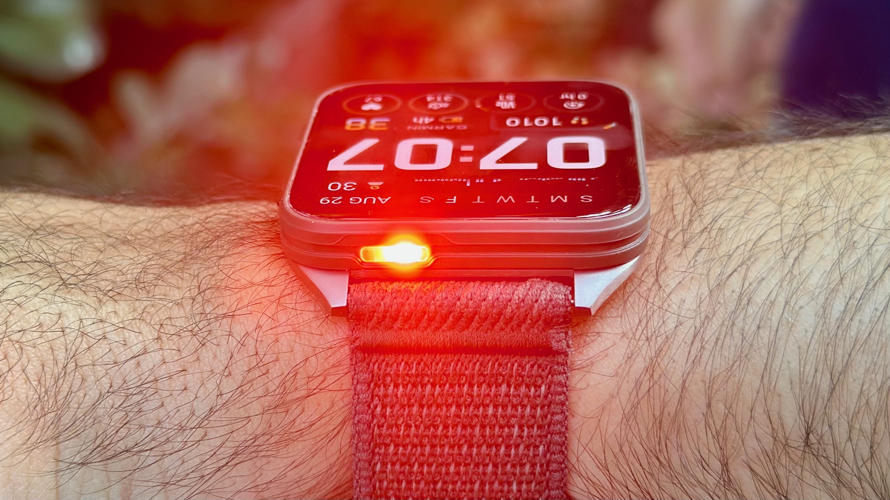 The Garmin Venu X1 on the author's wrist, the front pointed toward the camera with the red LED flashlight activated and glowing faintly.