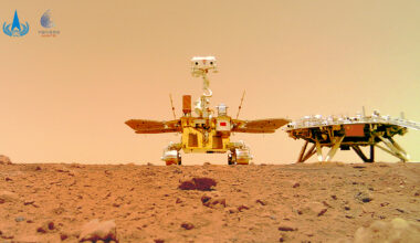 A photo of a metal rover with wheels and two solar panels standing on reddish brown dirt.