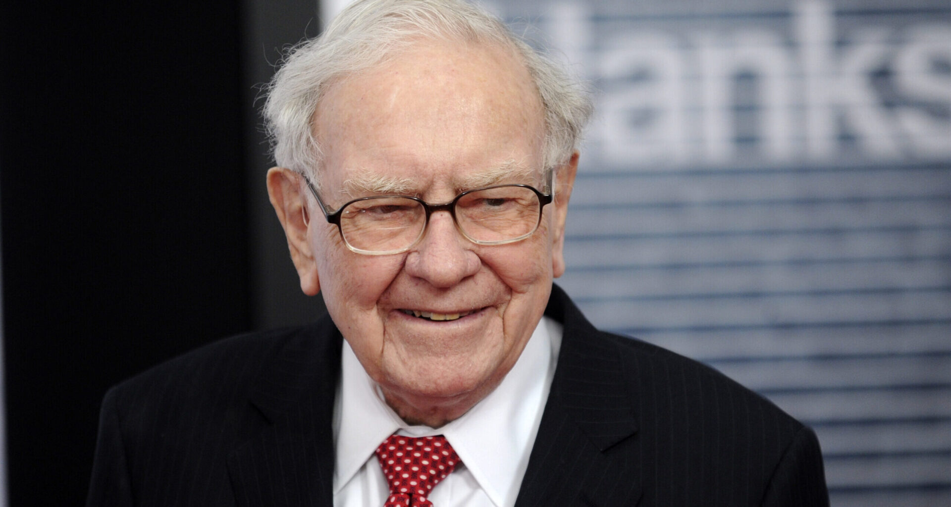 Warren Buffett, wearing a striped black suit jacket and a red tie, is seen smiling at the Newseum in Washington, D.C.