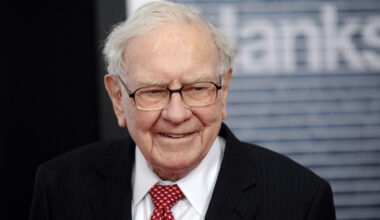 Warren Buffett, wearing a striped black suit jacket and a red tie, is seen smiling at the Newseum in Washington, D.C.